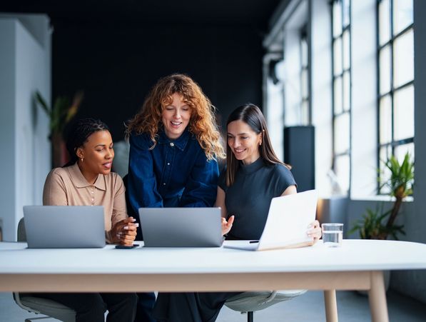 Three women collaborating on laptops in a bright office space.