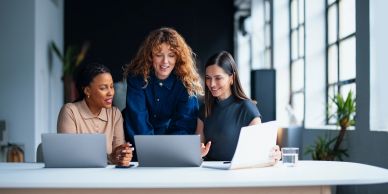 Three women collaborating over laptops in a modern office.