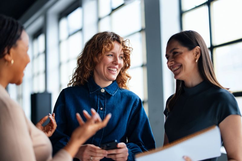 Team of professional women engaging in a friendly meeting, promoting teamwork and collaboration within a modern office environment.