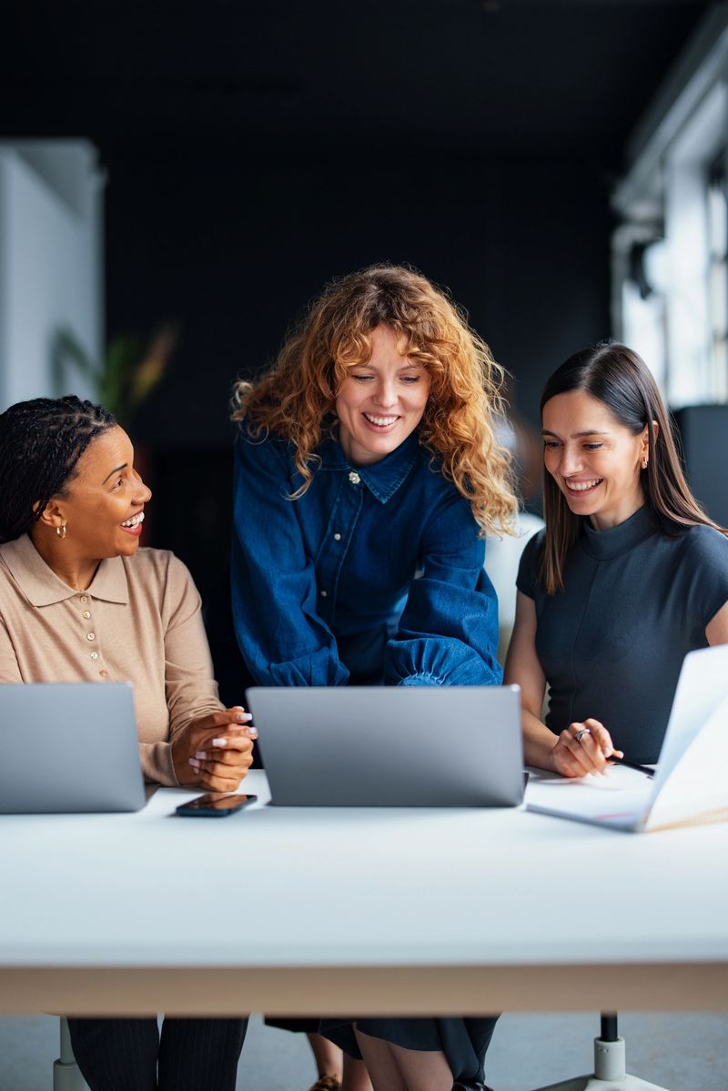 Professional women discussing a project on laptops, showcasing teamwork, collaboration, and a modern office environment, emphasizing productivity and cooperation in a business setting.