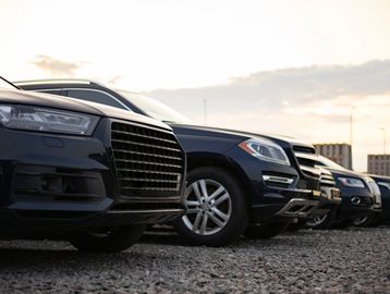Line of black SUVs parked on gravel during sunset.