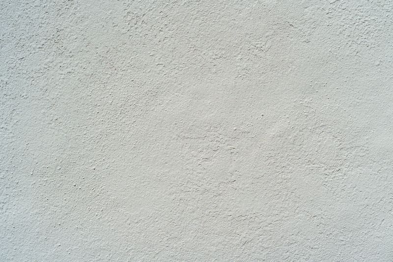 A detailed close-up of a white stucco wall with subtle rough texture, capturing the natural imperfections of a plastered surface.