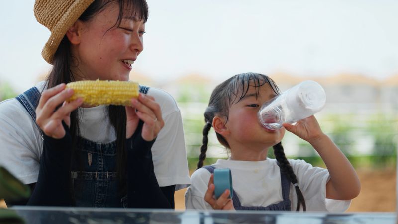 A mother and her small daughter is taking a break from working in the farm and eating raw corn that they just newly harvested in their farmland.