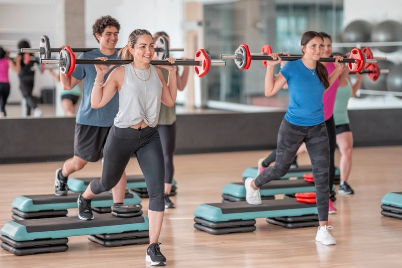Energetic people in a fitness class practicing barbell lunges, focusing on health and teamwork in a modern gym. Vibrant scene highlighting exercise, determination, and physical fitness in an interactive group exercise environment.