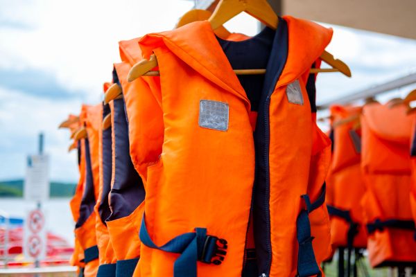 Bright orange life jackets hanging on wooden hangers.