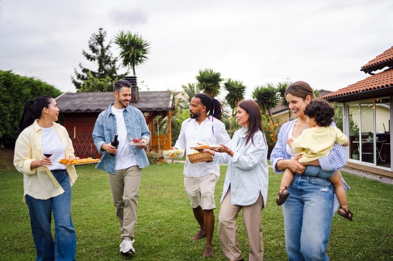 Diverse friends mingling on green lawn, sharing food, drinks during casual outdoor social gathering with camaraderie and relaxed atmosphere