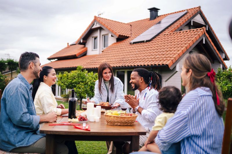 Group of diverse friends enjoying a delicious meal together in the backyard of a sustainable home, featuring solar panels on the roof