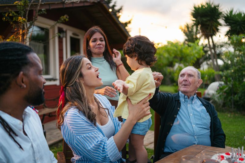 Multicultural family enjoying outdoor gathering, smiling toddler joining festive backyard moment