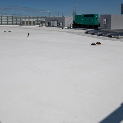 Flat white rooftop with HVAC units and solar panels under a clear sky.