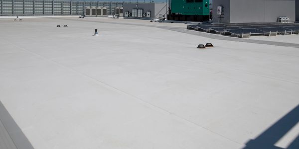Flat white rooftop with HVAC units and solar panels under a clear sky.
