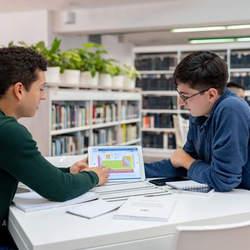 Two students studying chemistry using a tablet in a library.
