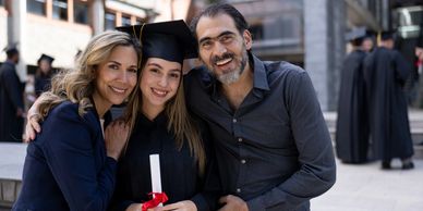 Happy graduate with proud parents celebrating graduation day outdoors.