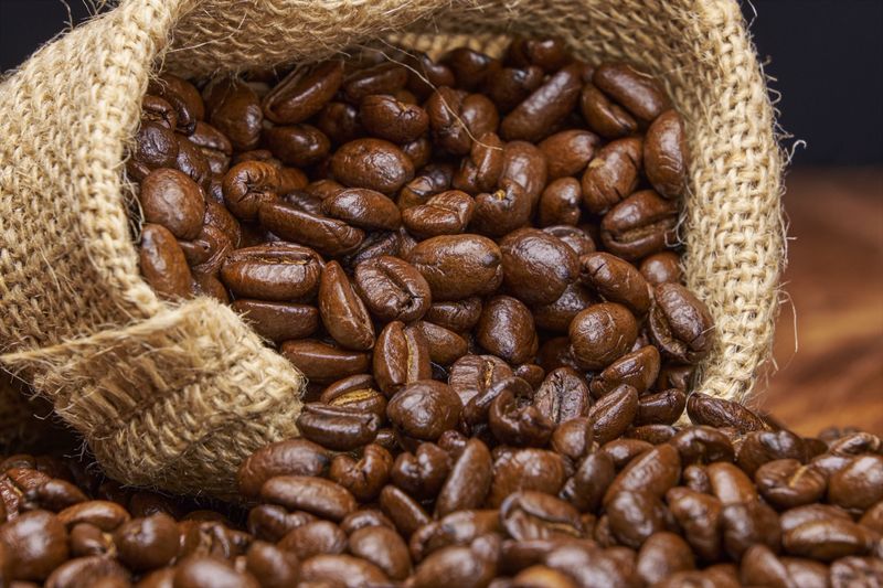 Roasted coffee beans spill from a jute bag onto a rustic wooden surface.