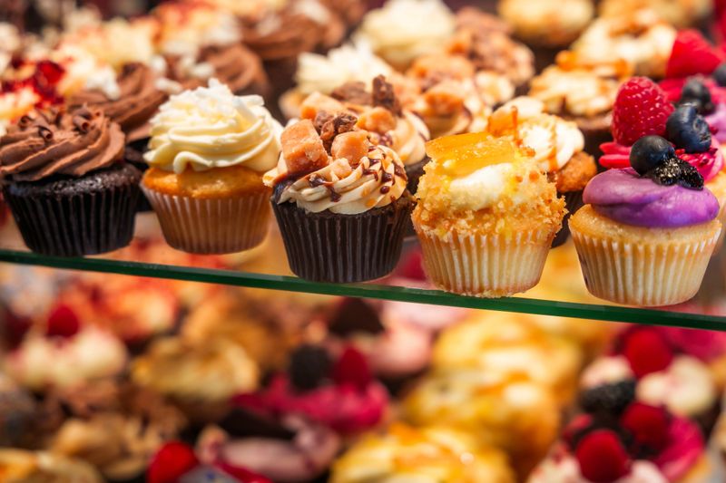 Close up color image depicting a selection of freshly baked delicious cakes and cupcakes displayed in a row at a food market. Room for copy space.