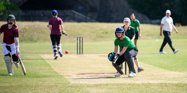 Women playing cricket on a grassy field.