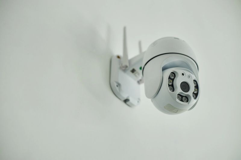Surveillance camera mounted on wall capturing security footage, showing modern wireless design with multiple infrared sensors and antennas, isolated against plain background