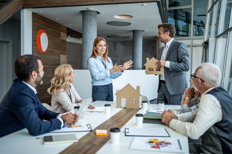 Real estate agents holding models of houses while presenting a new housing project to potential investors during a meeting in a modern office conference room