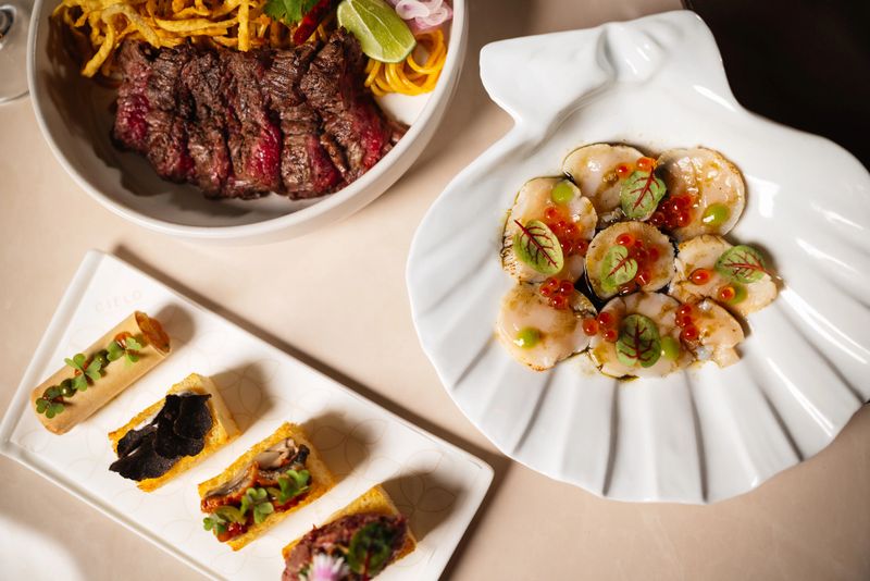 Overhead view of a table displaying a variety of gourmet dishes, including scallops, beef, and assorted canapés in a restaurant.