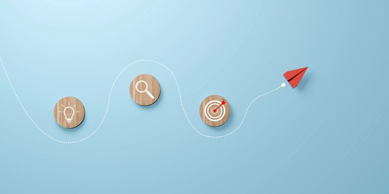 Business strategy and goal achievement, represented by a red paper plane flying along a dotted path through a wooden circle with icons symbolizing leadership and business goals achievement and success
