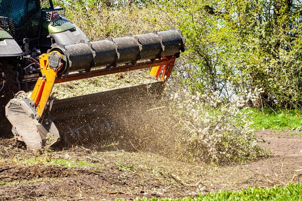 A tractor mulching branches and debris in a garden area.