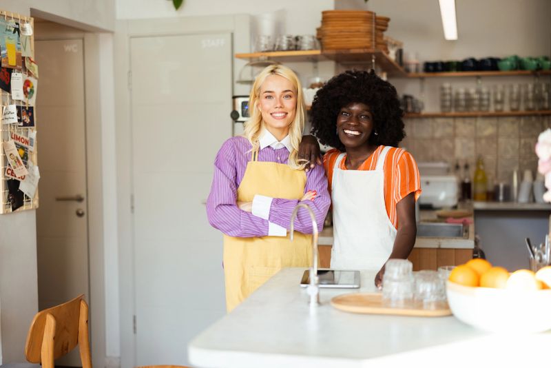 Two young waitresses are smiling and posing together in their cafe