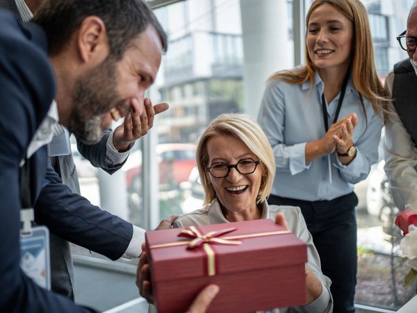 Colleagues happily presenting a gift to a smiling woman in an office setting.