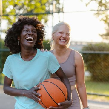 Two women laughing with a basketball outdoors.