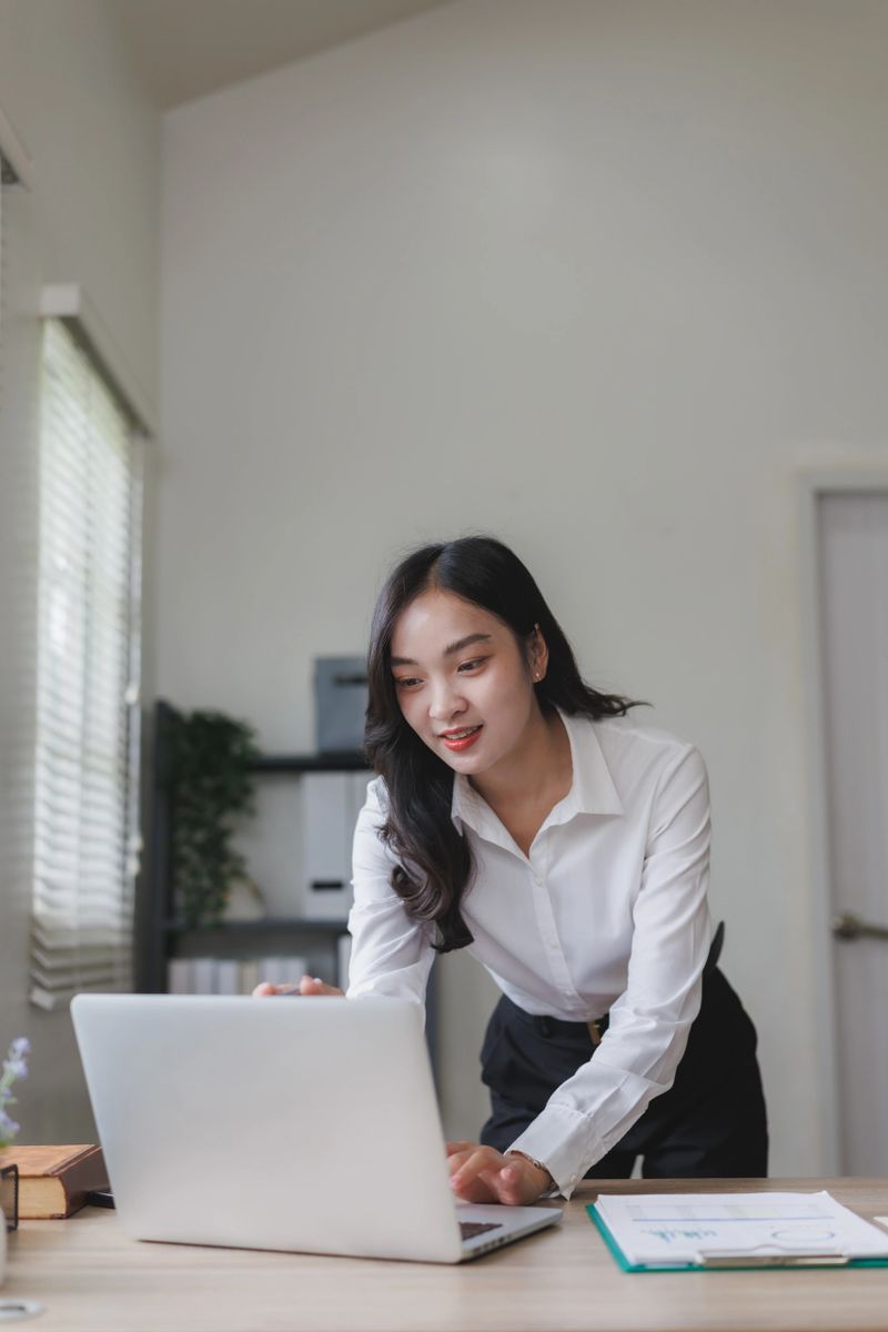 Young asian businesswoman concentrating on her laptop while working in a bright, modern office filled with natural light and organized spaces