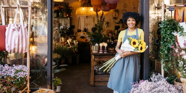 Smiling florist holding sunflowers in front of flower shop.