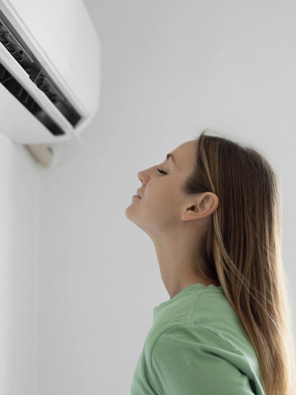 Woman enjoying cool air from an air conditioner on a hot day.