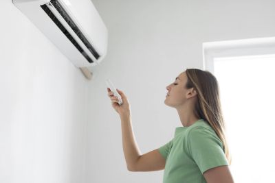 Woman adjusting air conditioner with remote.