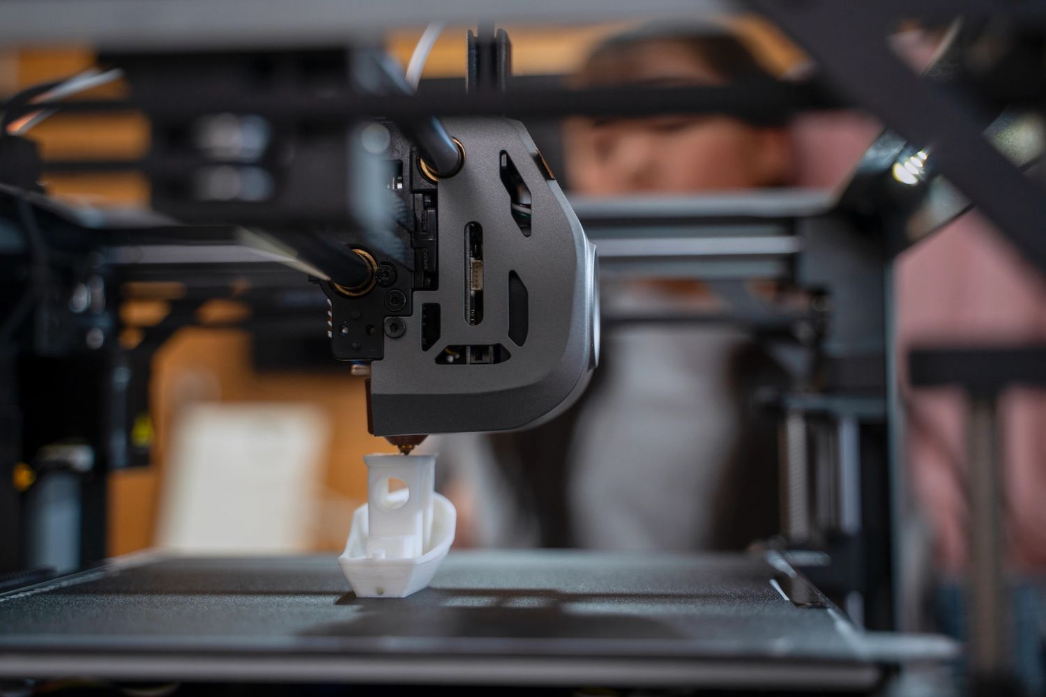 Close-up of a 3D printer creating a small white object with a person watching.
