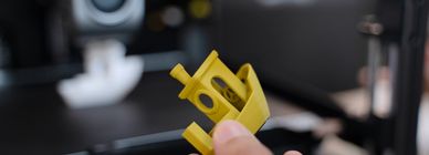 Close-up of a hand holding a small yellow 3D printed object.