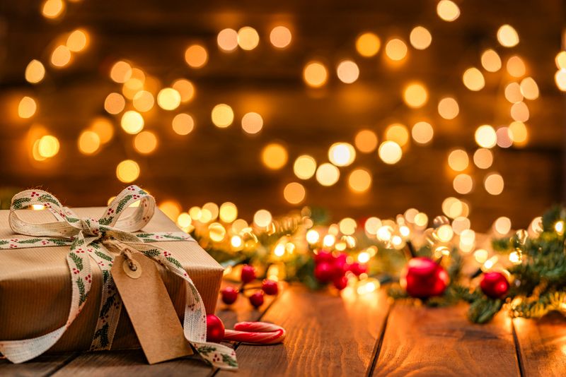 Christmas gift box with a blank tag wrapped with brown craft paper in a cozy festive atmosphere with defocused string lights and ornaments at background