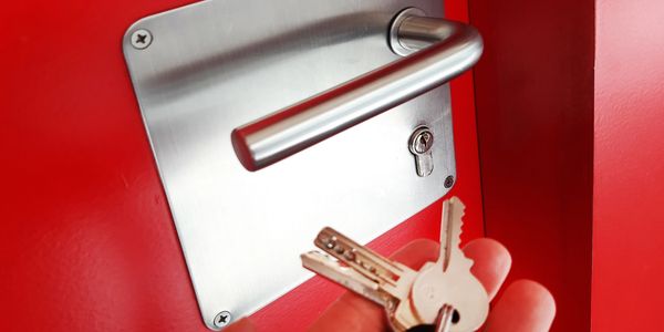 Hand holding keys near a silver door handle on a red door.