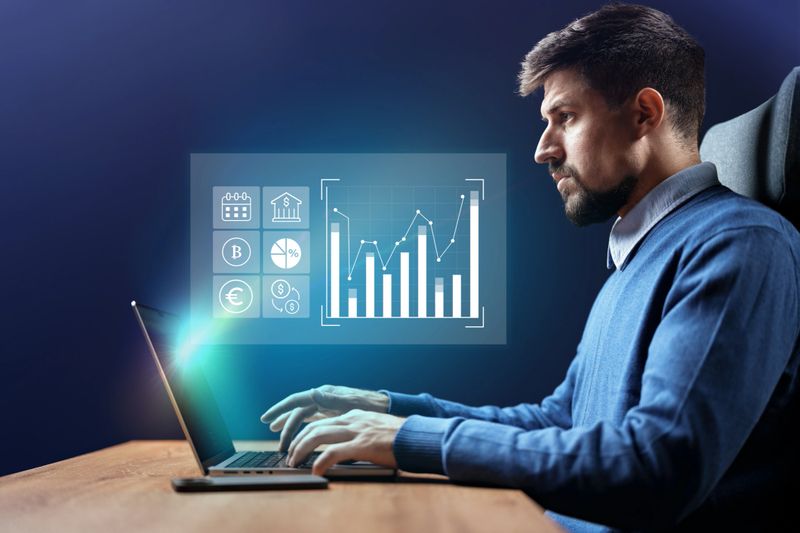 A focused individual analyzes financial data on a laptop. Graphs and icons reflecting market trends are displayed beside him, emphasizing the importance of analytics in business strategy.