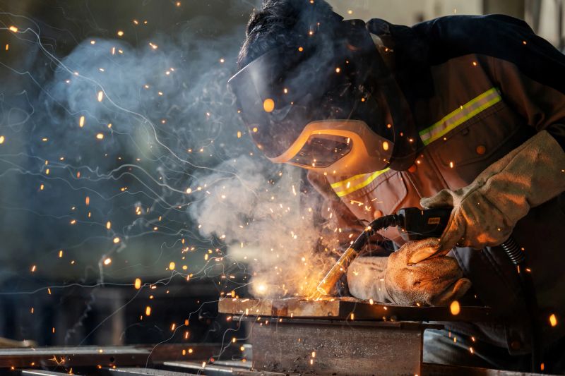 A skilled metalworker focuses intently while welding steel with a torch, dressed in heat-resistant coveralls and gloves. The glowing sparks highlight the energy and precision of industrial manufacturing.