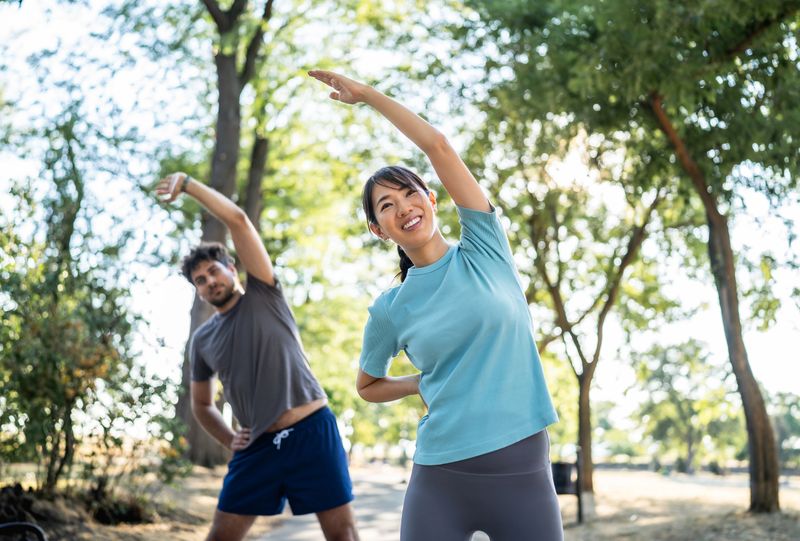 Young multi-ethnic couple stretching together in a sunlit park, preparing for their daily workout and enjoying a healthy, active lifestyle