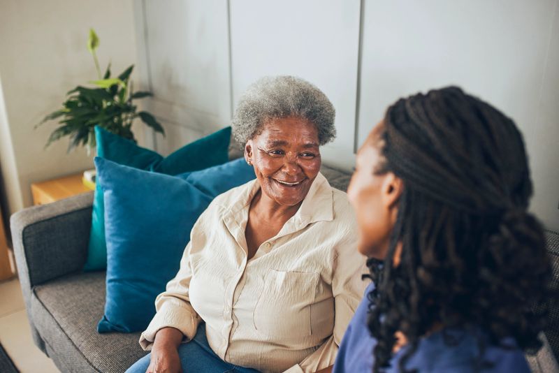 Portrait of senior woman smiling and having a happy conversation with young in house nurse on sofa at home