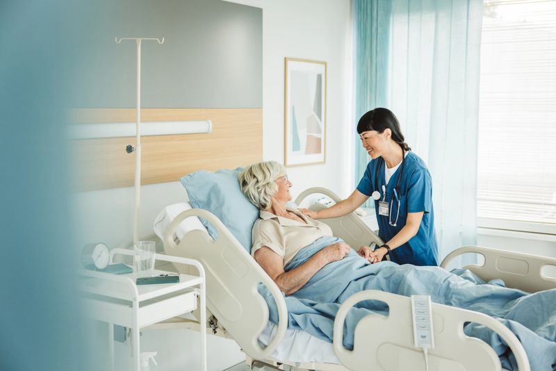 Nurse talking to senior woman in hospital bed. She is showing empathy for her condition.