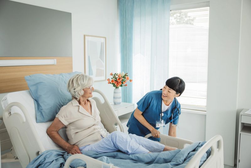 Nurse talking to senior woman in hospital bed. She is showing empathy for her condition.