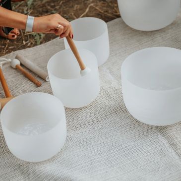 Person playing white crystal singing bowls with a wooden mallet.