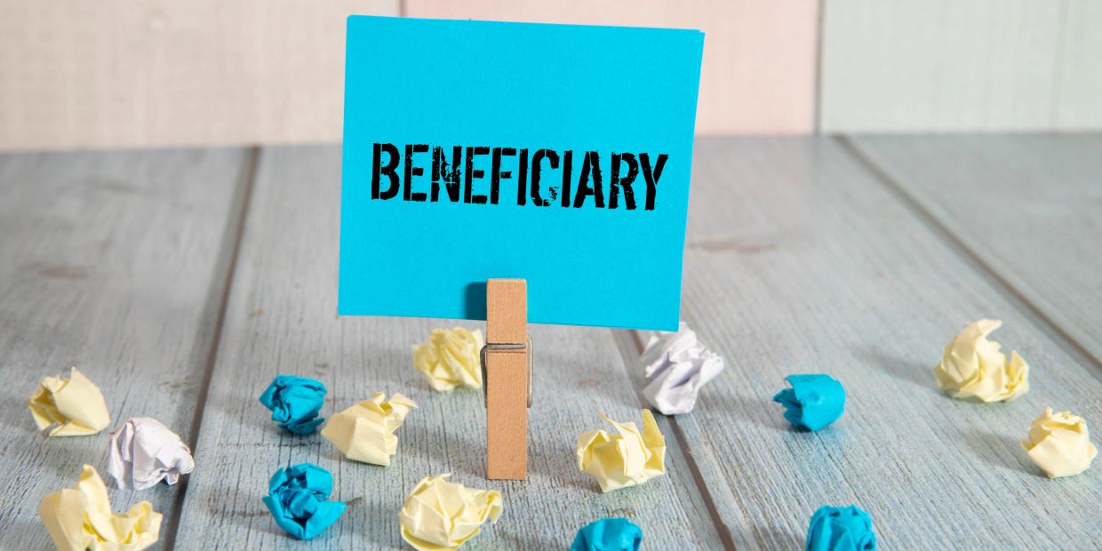 The word Beneficiary being held on a post it note by a close pin surrounded by crumpled up sticky no