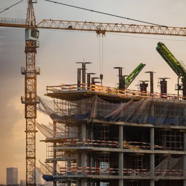 A building under construction with cranes during sunset.