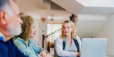 Three people having a conversation at a table with a laptop.