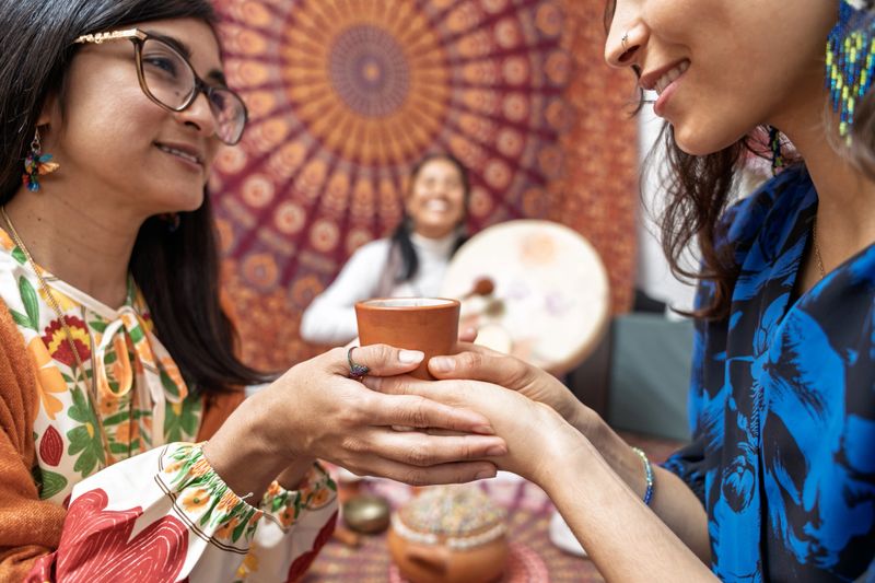 Women sharing a moment of connection during a traditional cacao ceremony, holding a clay cup and smiling