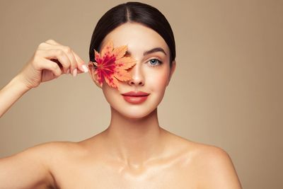 Woman holding an autumn leaf over one eye.
