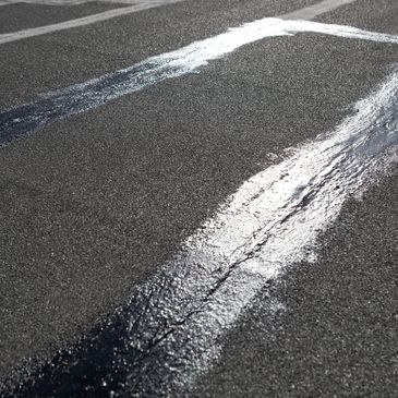 Fresh tar sealant filling cracks on an asphalt road surface.