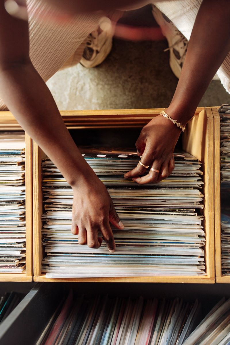 Top view of a young woman with warm-toned skin browses through vinyl records in a retro music store, wearing casual attire and jewelry, creating a nostalgic atmosphere