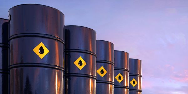 Row of black oil barrels with droplet symbol against the sky.